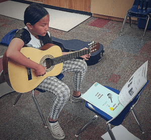 Young musician playing guitar looking at her guitar music.